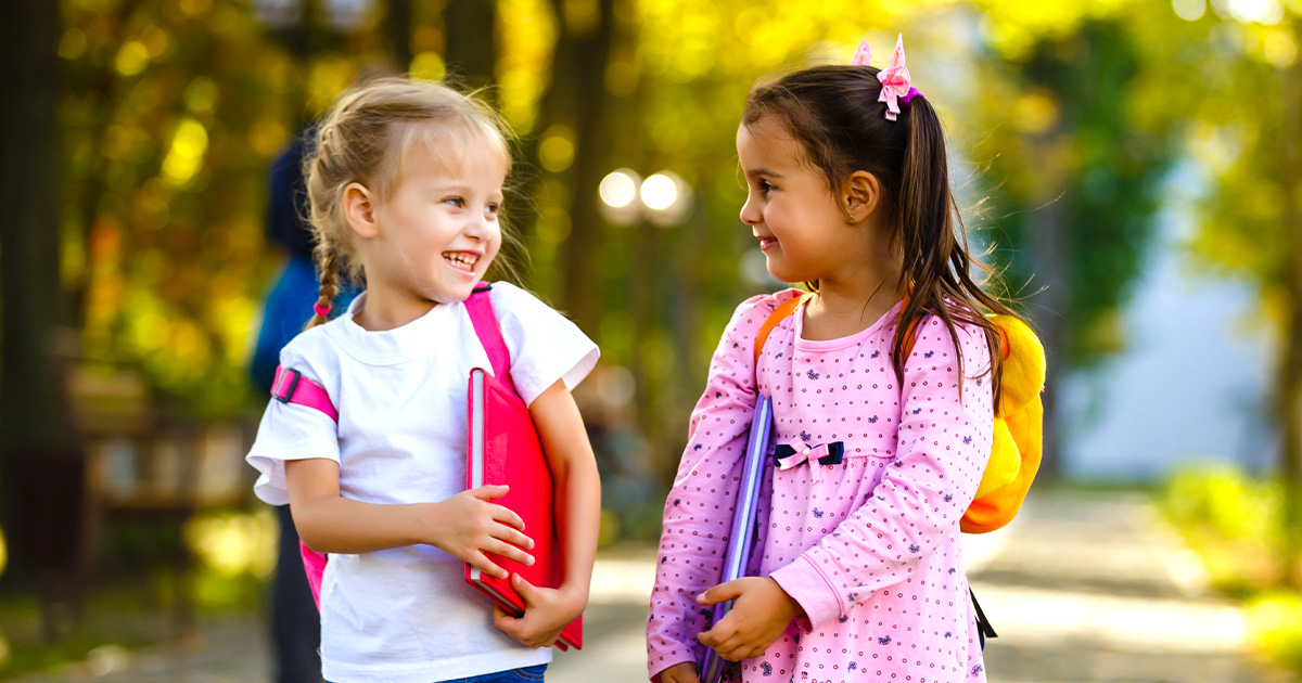 two young girls walking to school with backpacks on and folders in their hand